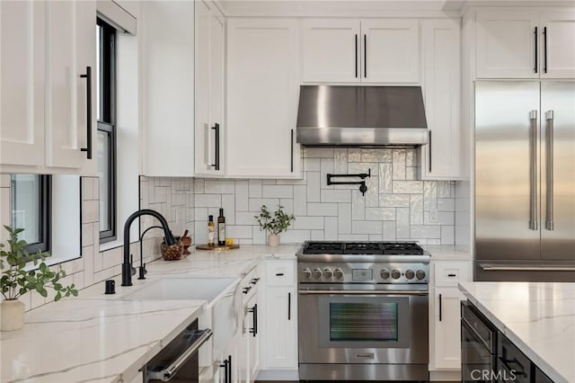 kitchen with high end appliances, white cabinetry, and range hood