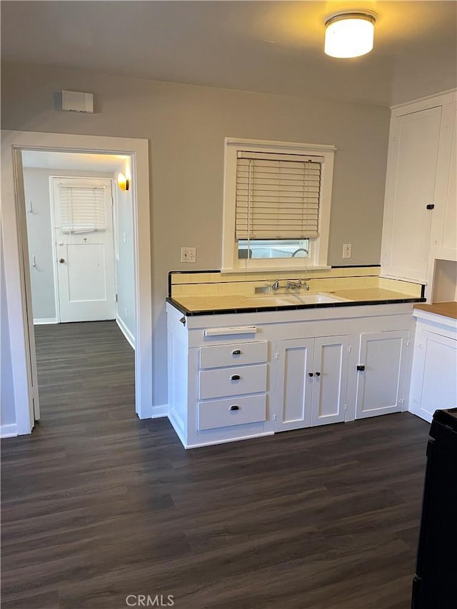 kitchen featuring dark wood-style floors, white cabinets, baseboards, and a sink