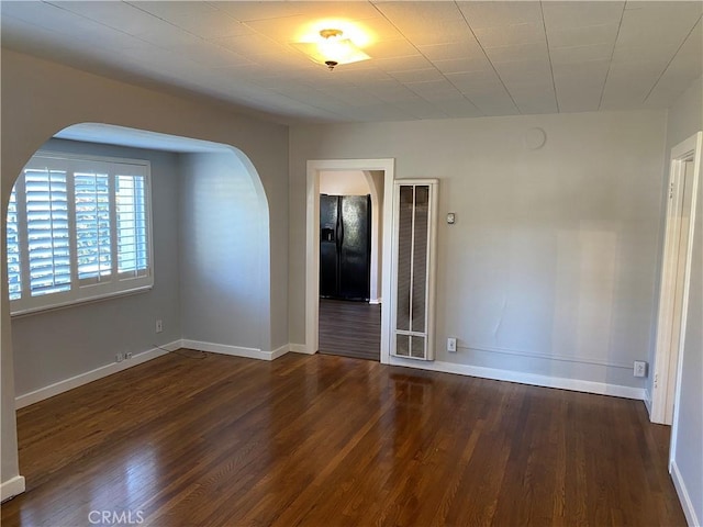 spare room with arched walkways, baseboards, and wood finished floors