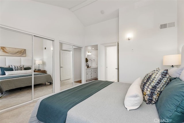 bedroom with multiple closets, ensuite bathroom, and high vaulted ceiling