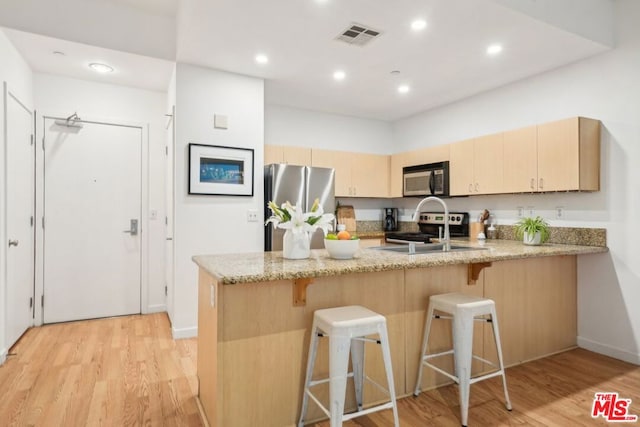 kitchen featuring light brown cabinetry, light hardwood / wood-style flooring, kitchen peninsula, stainless steel appliances, and light stone countertops