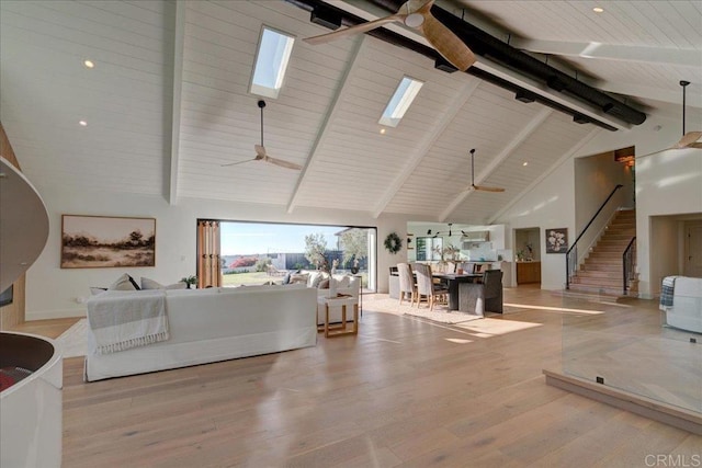 living room with ceiling fan, a skylight, high vaulted ceiling, beamed ceiling, and light wood-type flooring