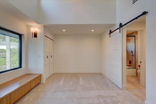 spare room featuring a barn door and light carpet