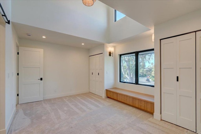 unfurnished bedroom featuring light carpet, two closets, and a towering ceiling