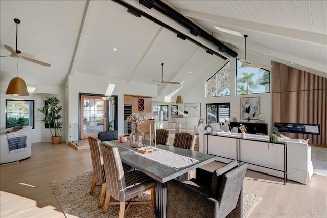 dining space with beam ceiling, ceiling fan, high vaulted ceiling, and wood walls