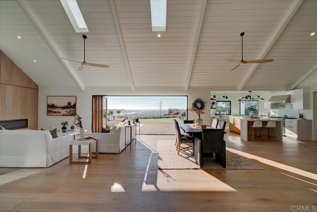 dining room with ceiling fan, wood-type flooring, wooden walls, and vaulted ceiling with skylight