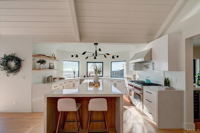 kitchen with wall chimney exhaust hood, range with two ovens, wooden ceiling, decorative backsplash, and white cabinets