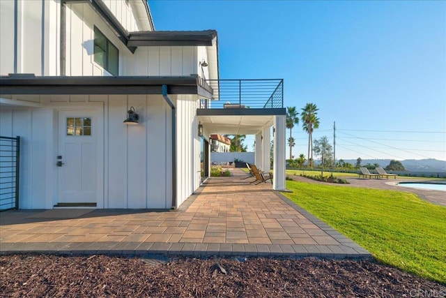 entrance to property featuring a yard, a patio area, and a balcony