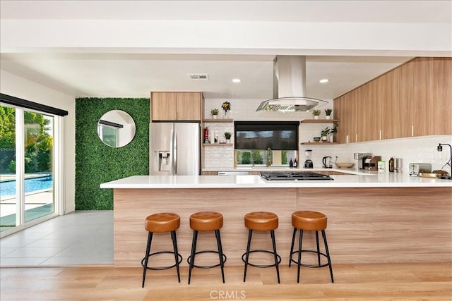 kitchen featuring light hardwood / wood-style flooring, a breakfast bar, appliances with stainless steel finishes, island range hood, and kitchen peninsula