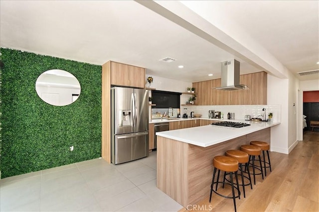 kitchen featuring sink, appliances with stainless steel finishes, island range hood, a kitchen bar, and kitchen peninsula