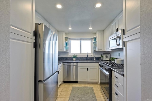 kitchen with light tile patterned flooring, appliances with stainless steel finishes, sink, and white cabinets