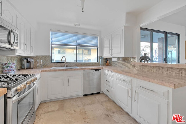 kitchen with stainless steel appliances, white cabinetry, sink, and backsplash