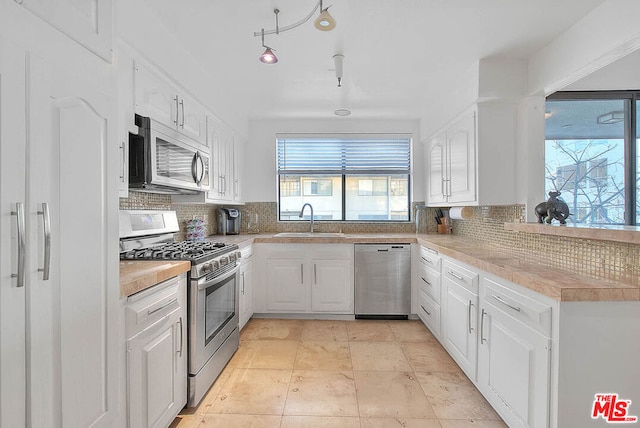 kitchen with appliances with stainless steel finishes, sink, white cabinets, and backsplash