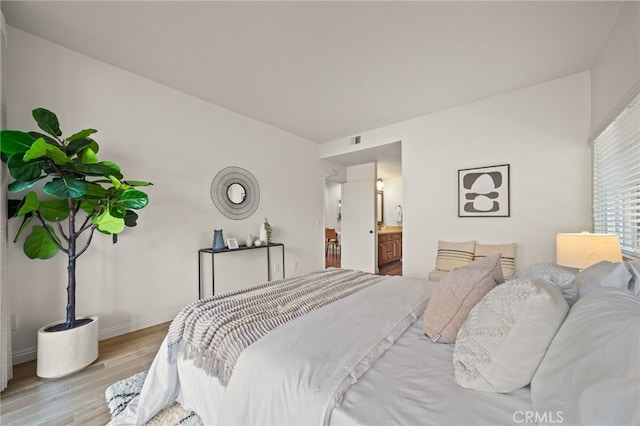 bedroom with ensuite bathroom and light hardwood / wood-style flooring