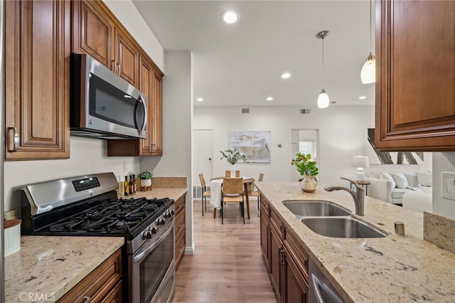 kitchen featuring sink, hanging light fixtures, stainless steel appliances, light stone countertops, and hardwood / wood-style floors