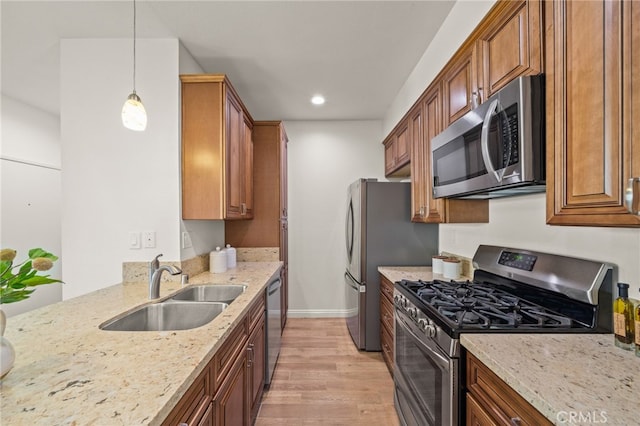 kitchen with sink, light stone counters, hanging light fixtures, appliances with stainless steel finishes, and light hardwood / wood-style floors