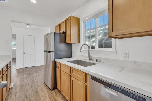 kitchen with sink, light hardwood / wood-style flooring, light stone countertops, and appliances with stainless steel finishes