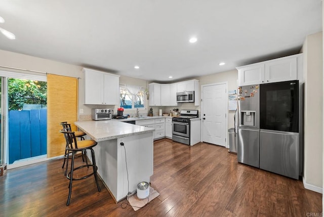 kitchen featuring appliances with stainless steel finishes, white cabinetry, a breakfast bar area, dark hardwood / wood-style flooring, and kitchen peninsula