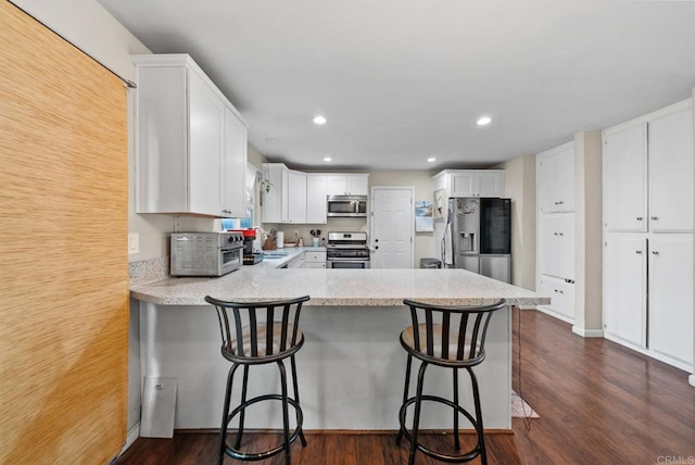 kitchen with dark wood-type flooring, a breakfast bar, white cabinetry, stainless steel appliances, and kitchen peninsula