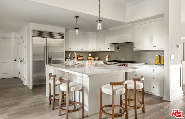 kitchen featuring pendant lighting, sink, white cabinetry, custom range hood, and stainless steel built in fridge