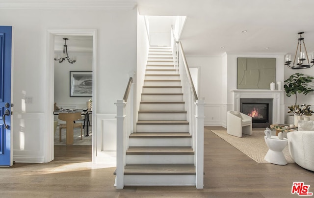 staircase with crown molding, wood-type flooring, and an inviting chandelier