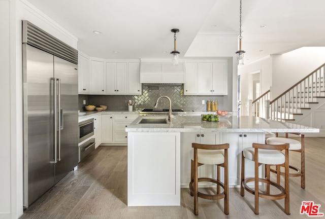 kitchen with built in appliances, white cabinetry, a kitchen island with sink, and custom range hood