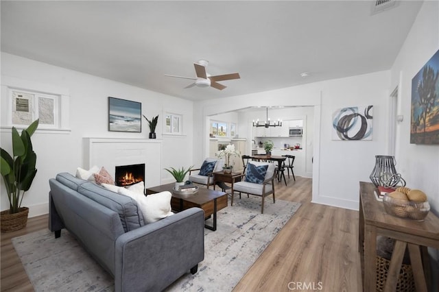 living room with ceiling fan with notable chandelier and light hardwood / wood-style flooring