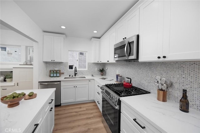 kitchen featuring sink, appliances with stainless steel finishes, white cabinetry, light stone counters, and tasteful backsplash