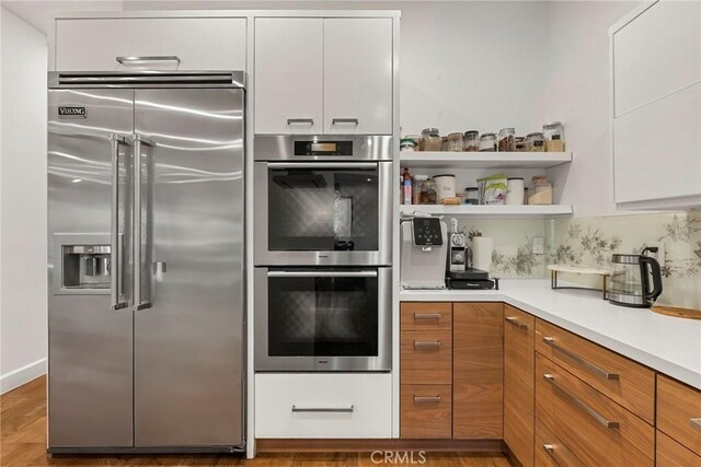 kitchen featuring white cabinetry, hardwood / wood-style floors, decorative backsplash, and appliances with stainless steel finishes