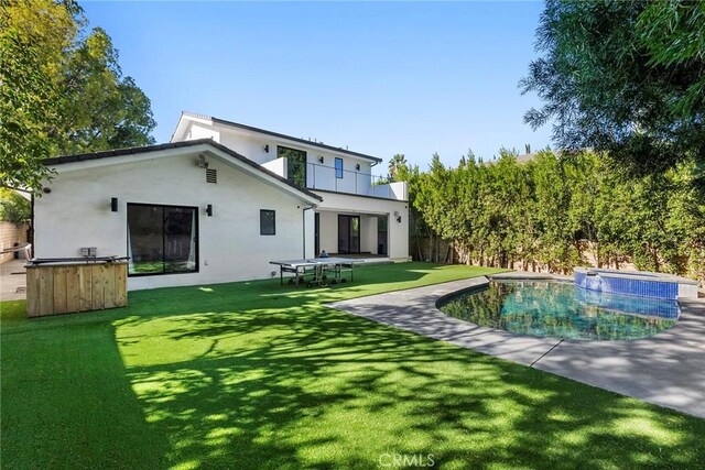 back of house featuring a balcony, a yard, and a swimming pool with hot tub