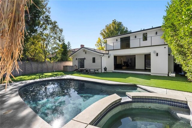 back of property with an in ground hot tub, a balcony, and a lawn