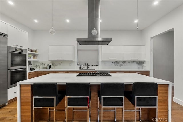 kitchen with tasteful backsplash, a center island, appliances with stainless steel finishes, island exhaust hood, and light stone countertops