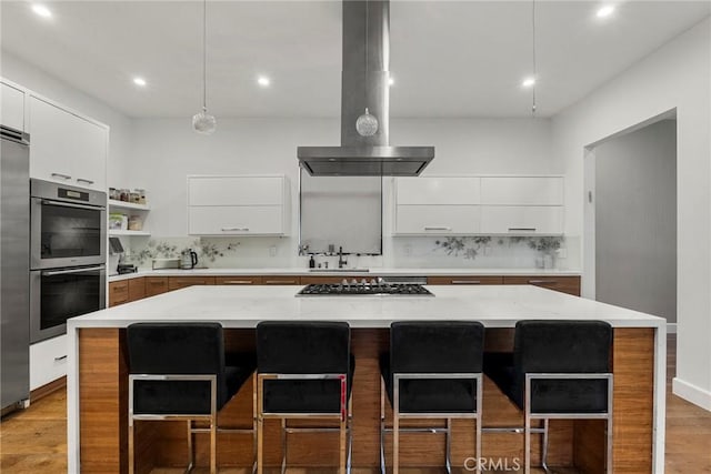 kitchen with appliances with stainless steel finishes, light stone counters, a center island, island range hood, and decorative backsplash