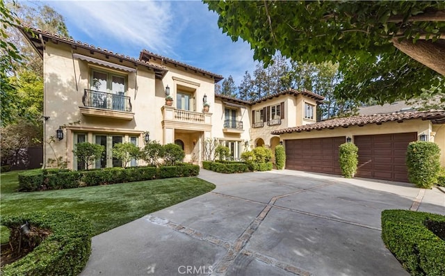 mediterranean / spanish home featuring driveway, a balcony, an attached garage, a front yard, and stucco siding