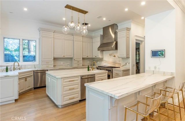 kitchen with appliances with stainless steel finishes, a breakfast bar area, a peninsula, wall chimney range hood, and pendant lighting