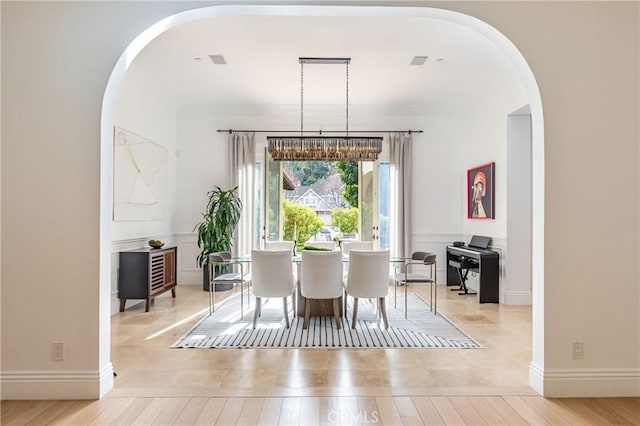 dining area with light wood-type flooring, a wainscoted wall, a decorative wall, and arched walkways