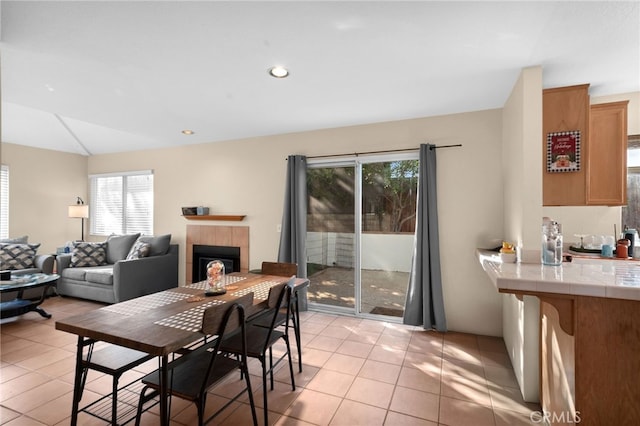 dining room featuring a wealth of natural light, a tiled fireplace, vaulted ceiling, and light tile patterned floors