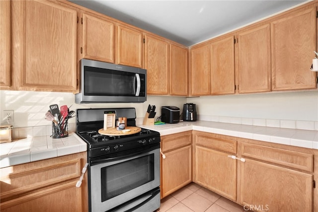 kitchen with appliances with stainless steel finishes, tile counters, light brown cabinets, and light tile patterned floors