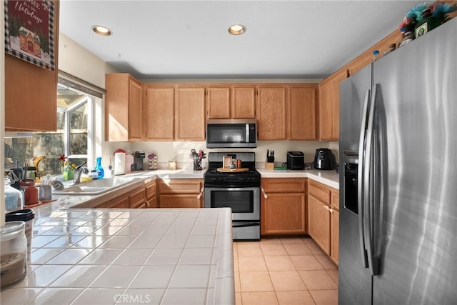 kitchen featuring light tile patterned flooring, appliances with stainless steel finishes, tile counters, and sink