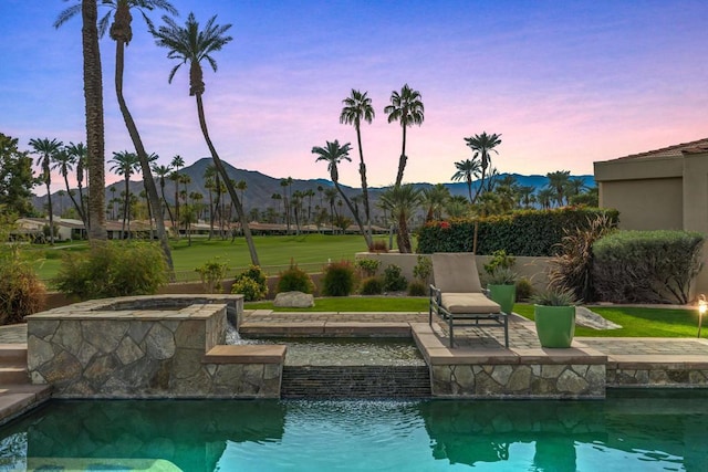 pool at dusk featuring an in ground hot tub, a mountain view, and a patio area