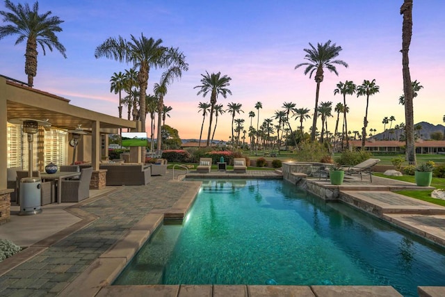 pool at dusk with a hot tub and a patio area