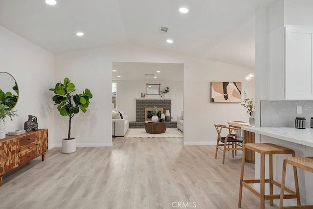 living room featuring lofted ceiling, a fireplace, and light hardwood / wood-style floors