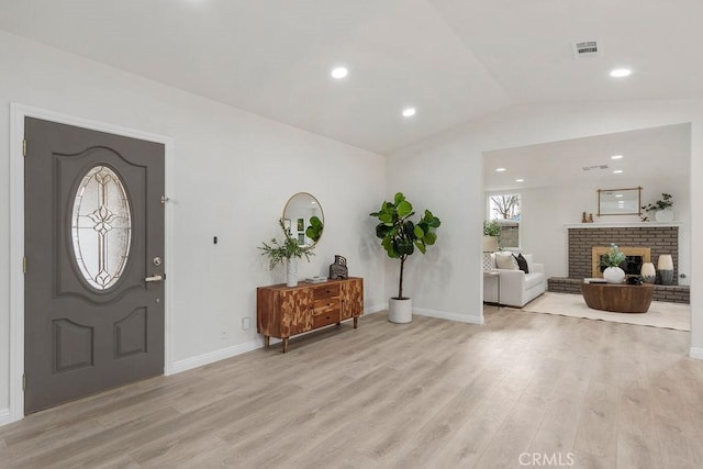 foyer entrance with light hardwood / wood-style floors, vaulted ceiling, and a brick fireplace