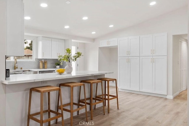 kitchen with light wood-type flooring, sink, a breakfast bar area, and white cabinets