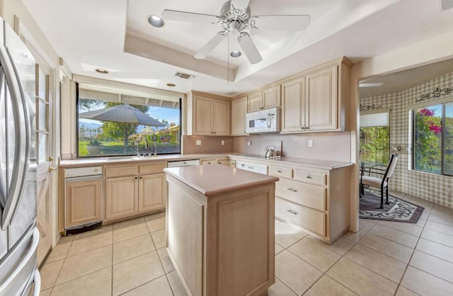 kitchen with a kitchen island, sink, stainless steel fridge, light tile patterned floors, and a tray ceiling