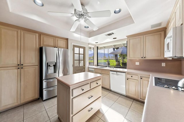 kitchen with light brown cabinetry, light tile patterned floors, a raised ceiling, a kitchen island, and white appliances