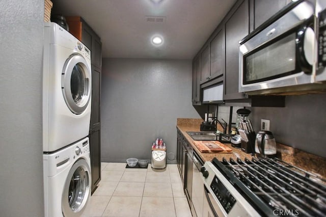 kitchen featuring light tile patterned flooring, stacked washer and dryer, appliances with stainless steel finishes, and sink