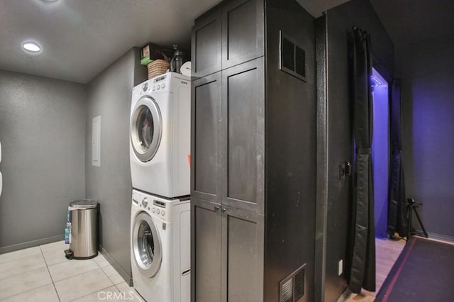 washroom featuring cabinets, stacked washer / drying machine, and light tile patterned floors