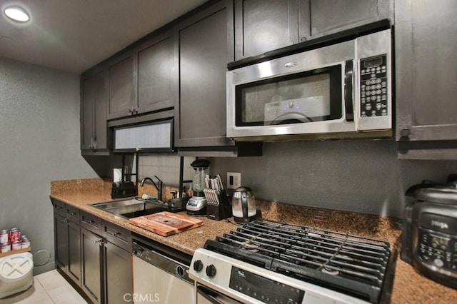 kitchen featuring sink, light stone counters, dark brown cabinets, light tile patterned floors, and stainless steel appliances