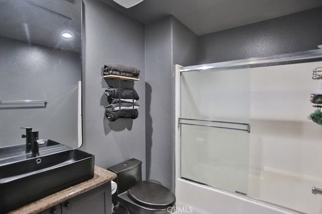 full bathroom with vanity, bath / shower combo with glass door, and toilet